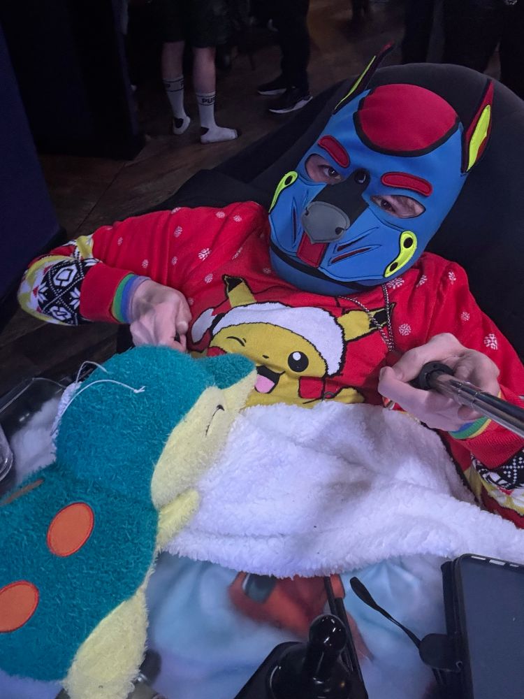 Disabled pup in a blue and red hood, wearing a red Pikachu Christmas jumper and a bright blue Pokémon Sherpa blanket. A Cyndaquil is resting on top of it