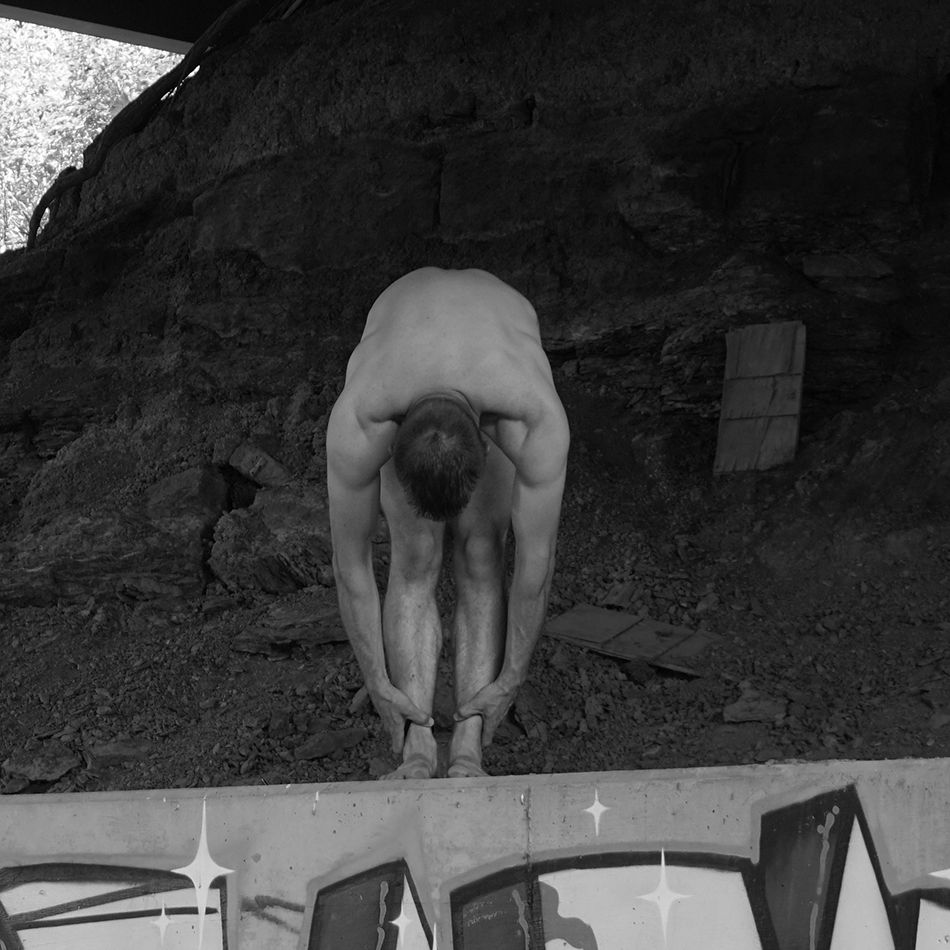 A black and white photo of me reaching toward my feet while standing on a bridge abutment.