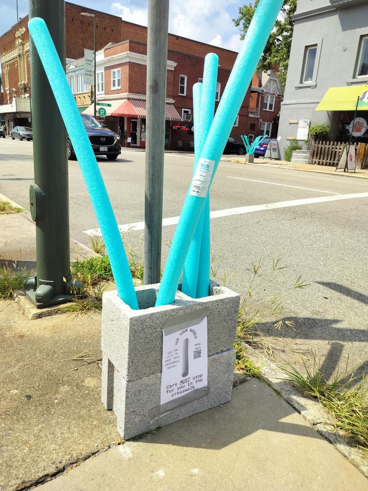 Two stacked cinder blocks full of pool noodles at a crosswalk.