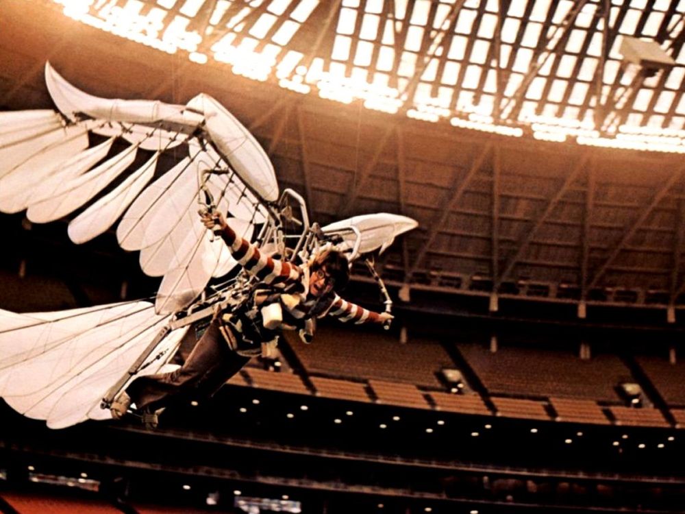 Bud Cort as Brewster McCloud, a bespectacled young man in a striped shirt strapped to giant wings and a tail, a mechanism that is enabling him to fly (he is above the ground, flapping, inside a large fieldhouse with stadium seating all around and light coming through the roof).