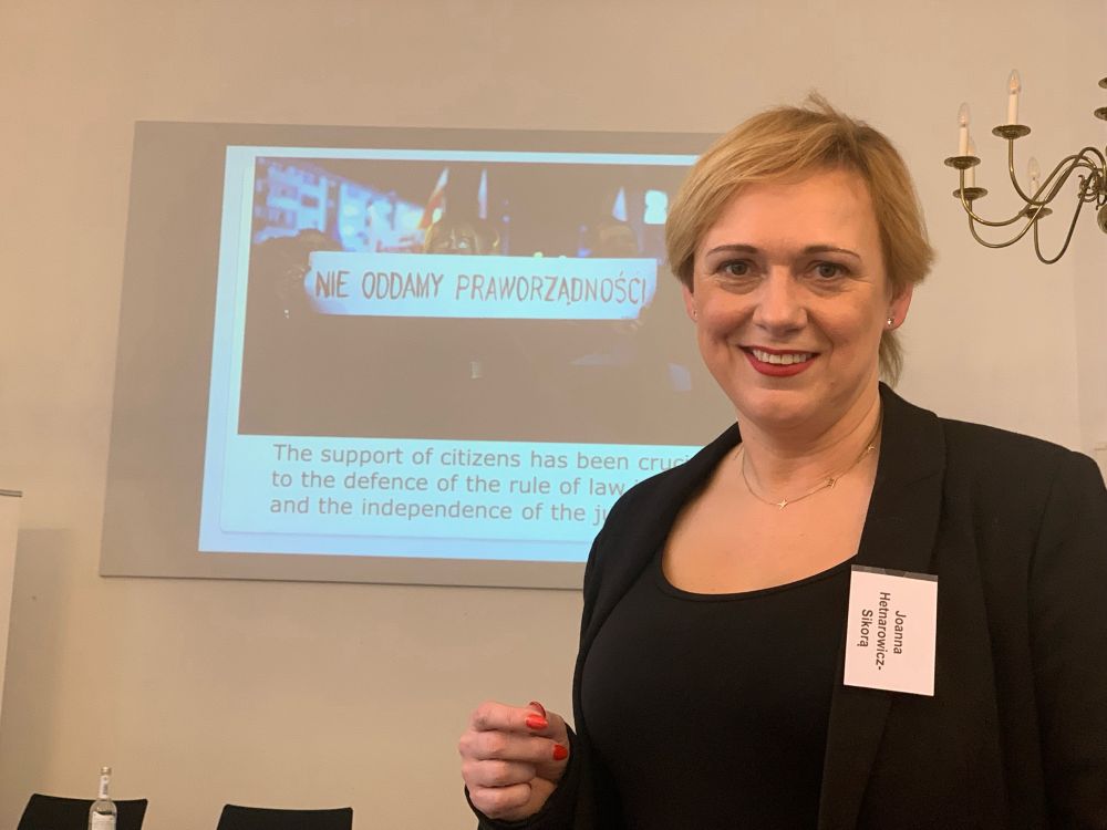 Richterin Joanna Hetnarowicz-Sikora im Porträt mit Power Point Präsentation von einer Demonstration im Hintergrund.