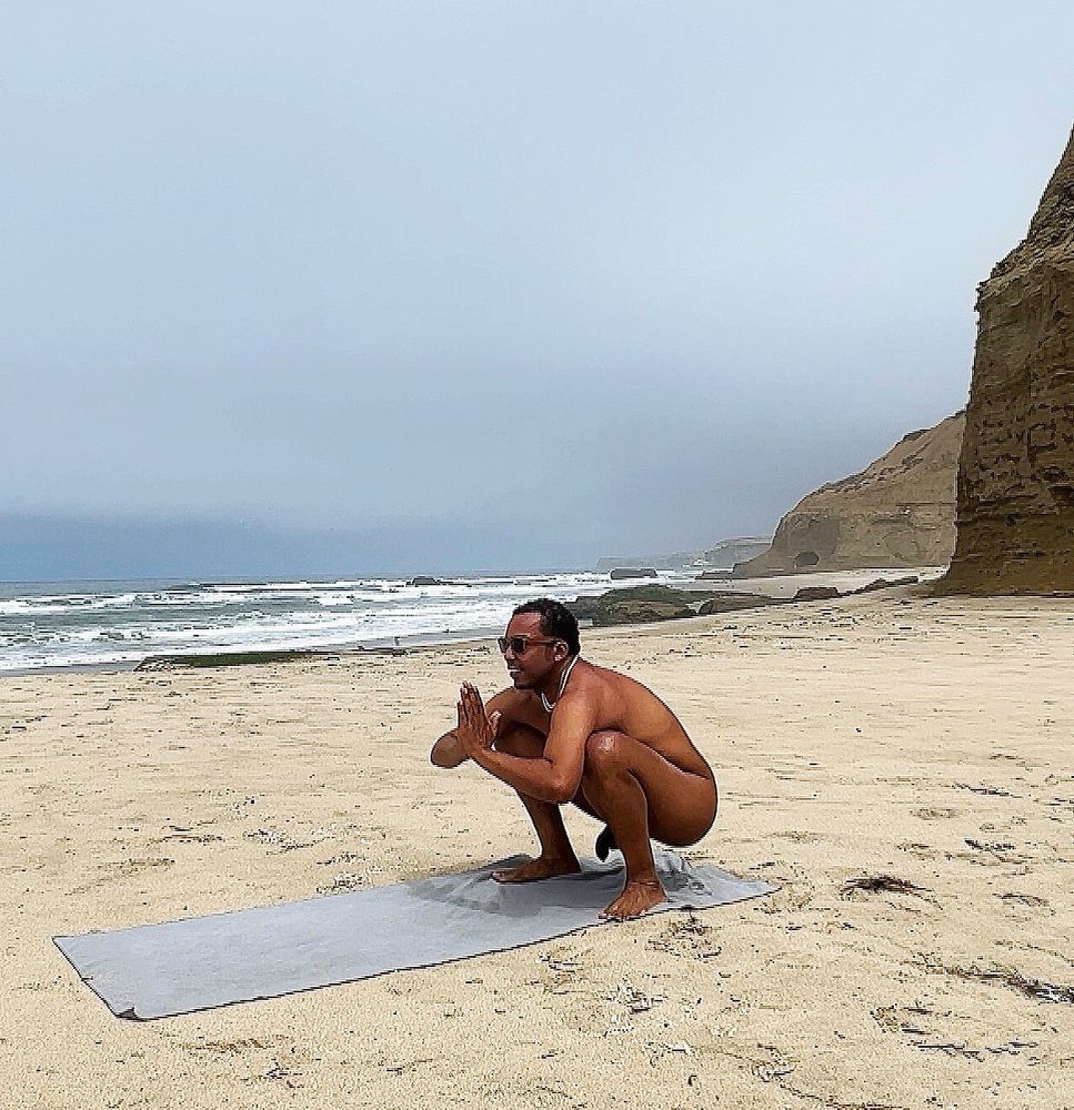 Sexy, naked, black gay man practicing yoga on the beach, on a grey, overcast day.