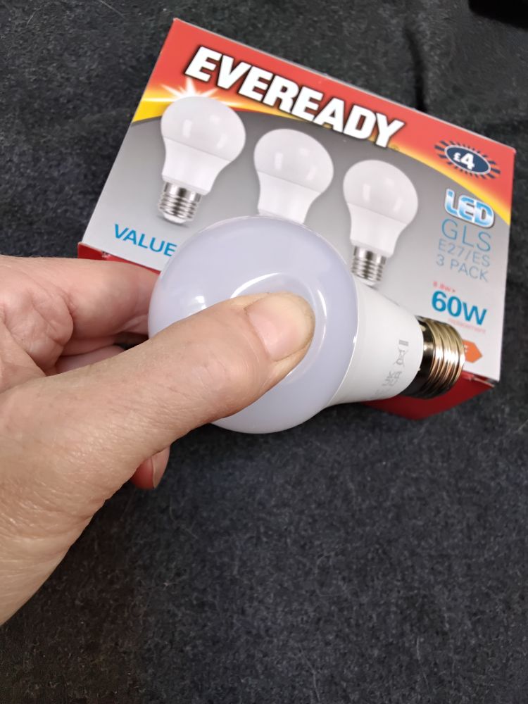 My thumb causing an indent in a white plastic light bulb with the box behind reading Eveready led 60w
