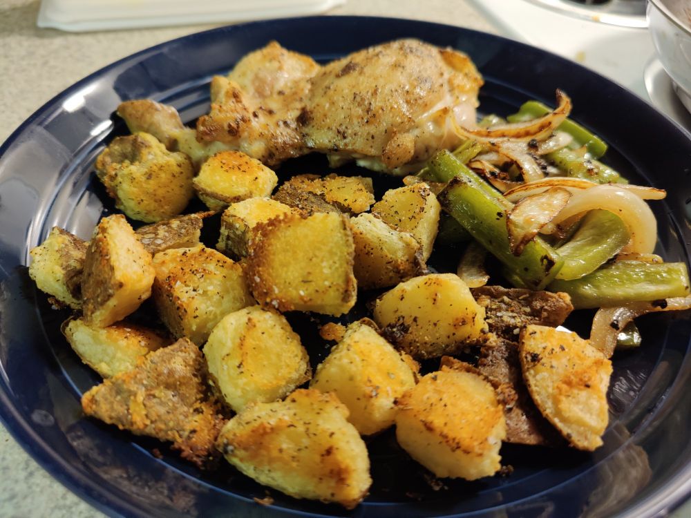 A dinner plate full of baked chicken, pan-fried veggies, and roasted potatoes in the focus. They're visibly crispy, but buttery and fluffy on the inside.