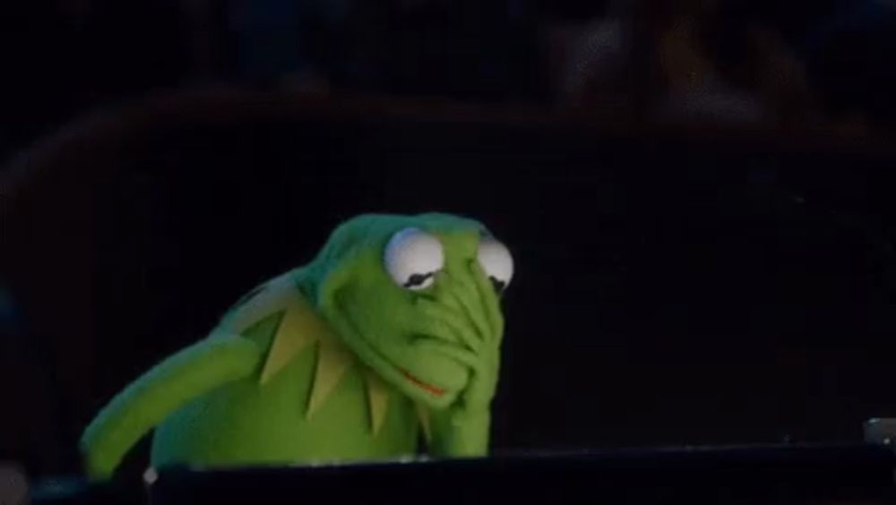 kermit the frog is covering his face with his hand in a dark room