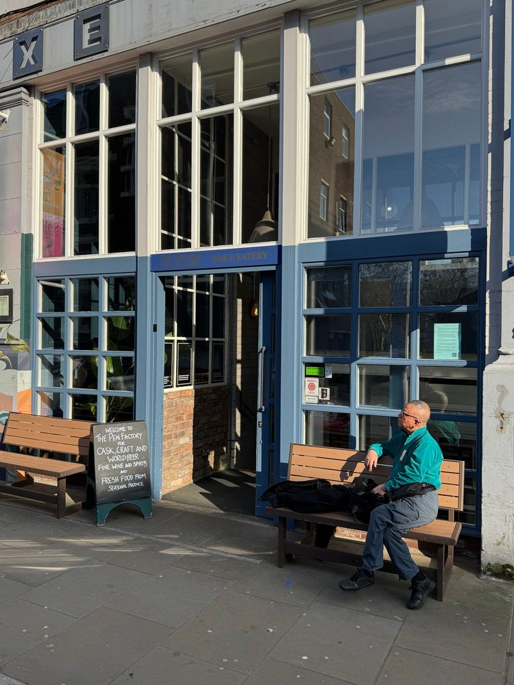 Man sat outside a cafe/bar in the sunshine. 