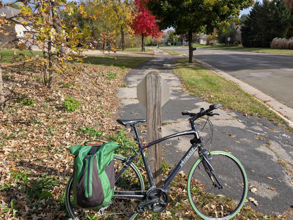 My bike leans against the back of a stop sign. Ahead there's a path paralleling the street, and a colorful tree canopy