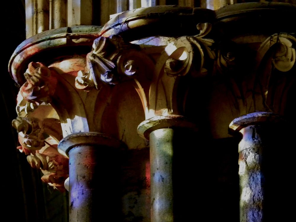 Mid thirteenth-century stiff-leaf capitals in the nave of Lincoln Cathedral, dappled with coloured light from stained glass windows.