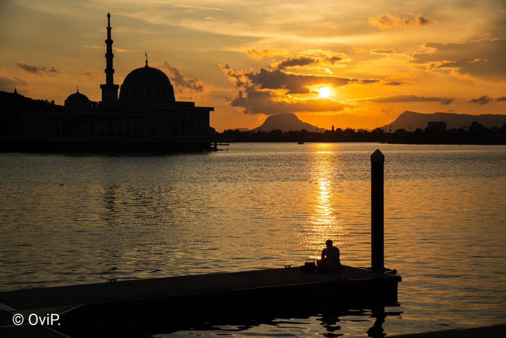 Sunset photo from Kuching, featuring a mosque and a man on a dock as sillhouettes.