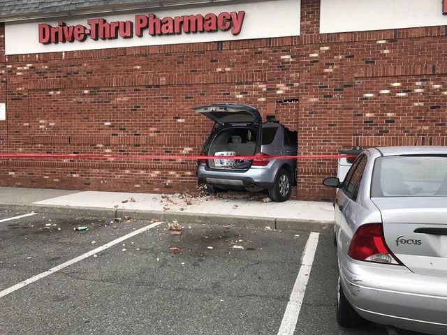 Picture of a wall with a crashed car lodged in the wall There is a business name at the top of the wall 