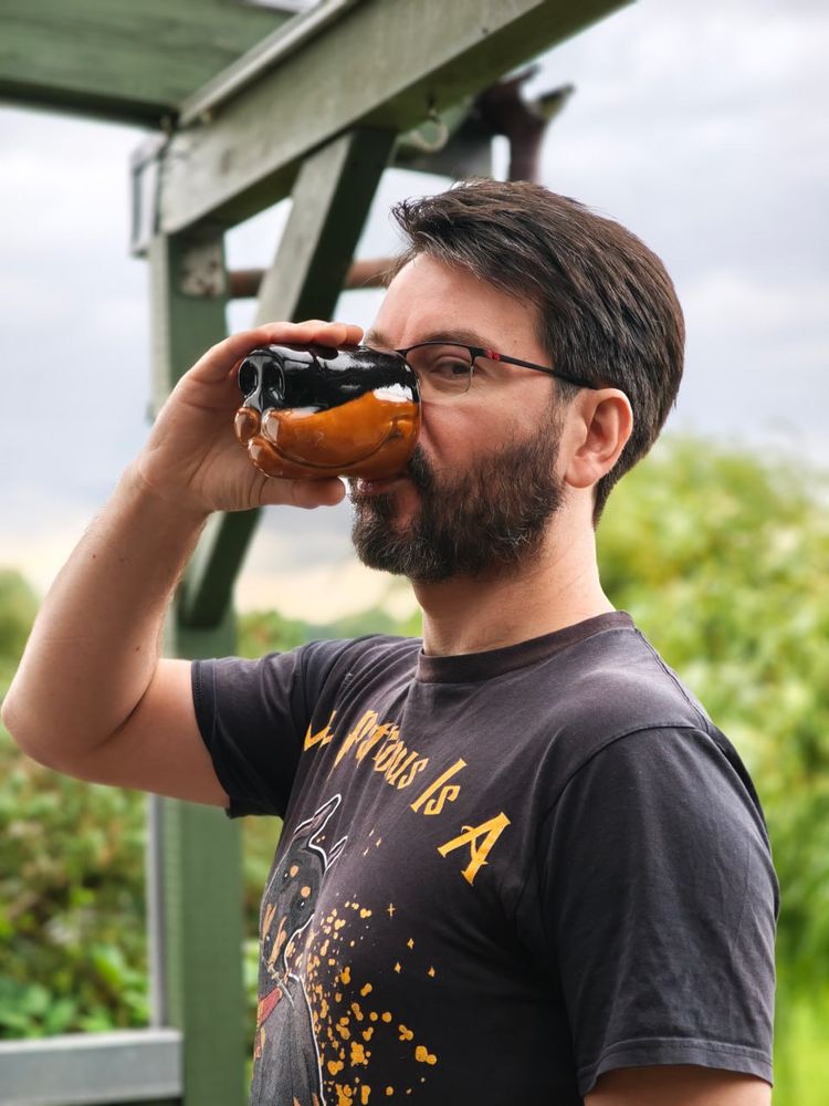 My husband posing with the canine snout shaped mug in front of some greenery. The mug is colored like a doberman, his fursona.