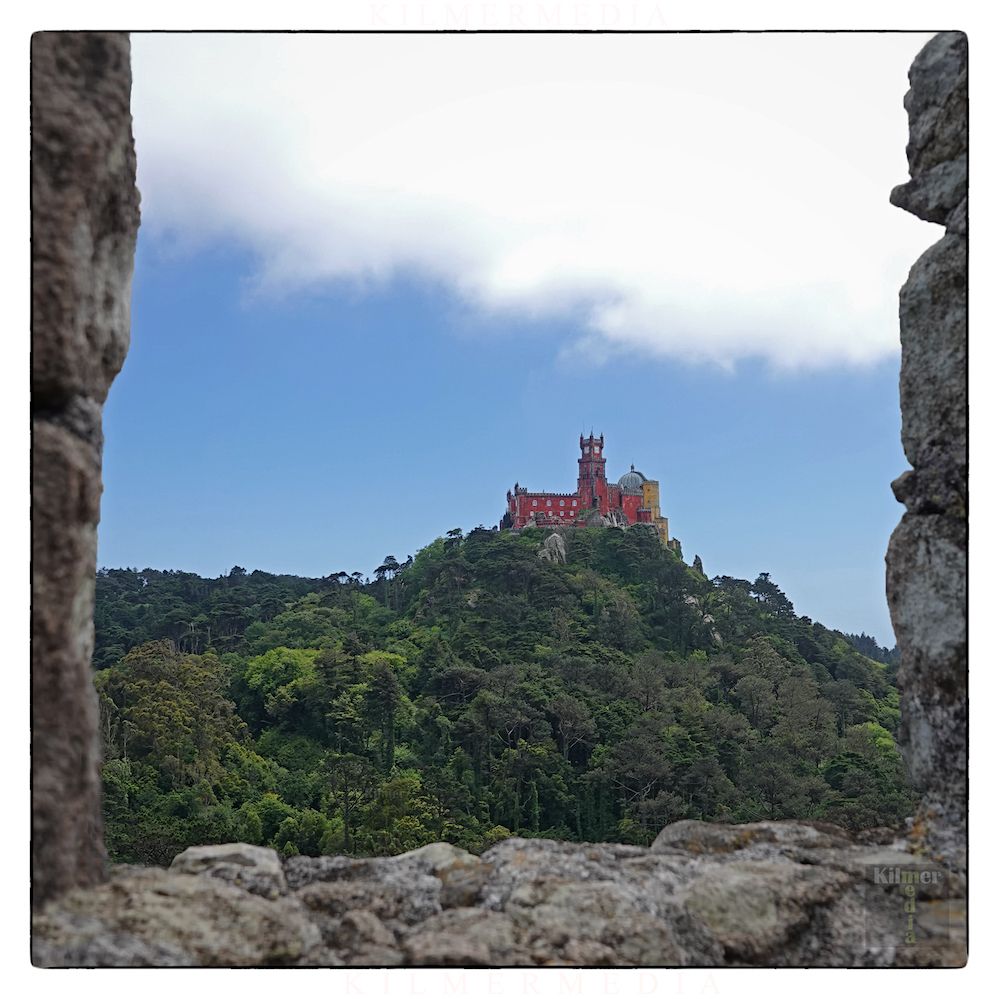 The colorful Pena Palace of Sinta, Portugal is shown during the day, viewed from the nearby Castle of the Moors.