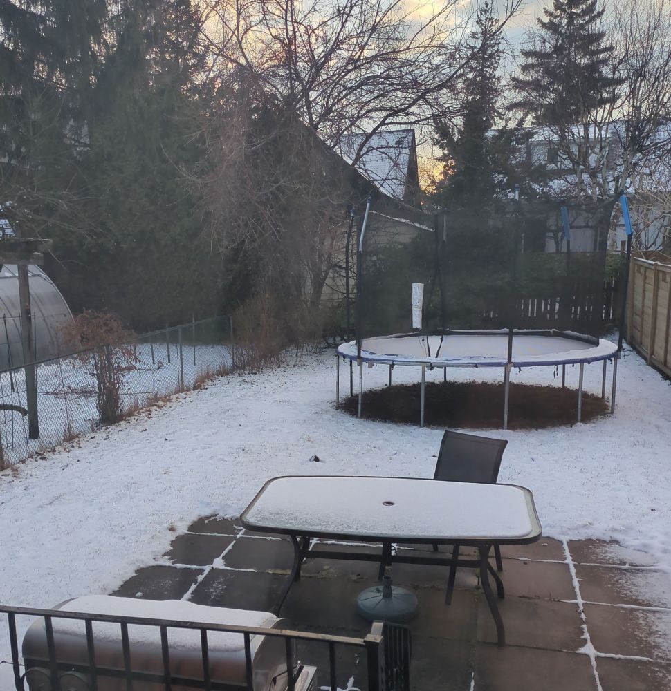 Photo of a backyard where the lawn, patio furniture, and trampoline are dusted with snow. 