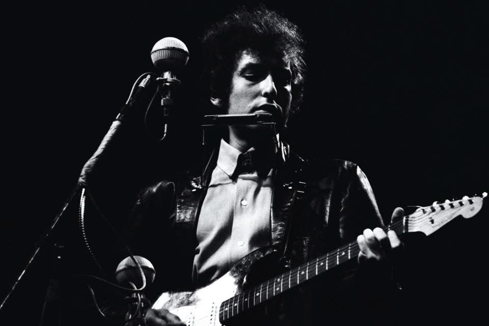 Bob Dylan playing a Fender electric guitar and harmonica at Newport.