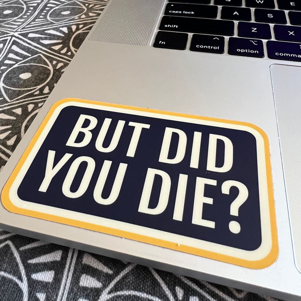 A closeup photo of a MacBook keyboard with a sticker affixed to it that reads “BUT DID YOU DIE?”