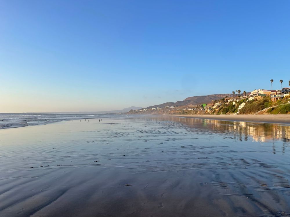 A negative low tide pulls the water way back, exposing the wet beach which reflects the sky, the colors and the buildings. 