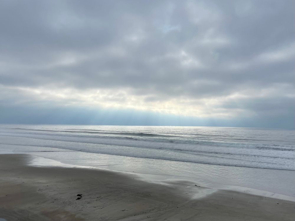 Light pouring through a thick cloud layer, illuminates the surface of the ocean. 