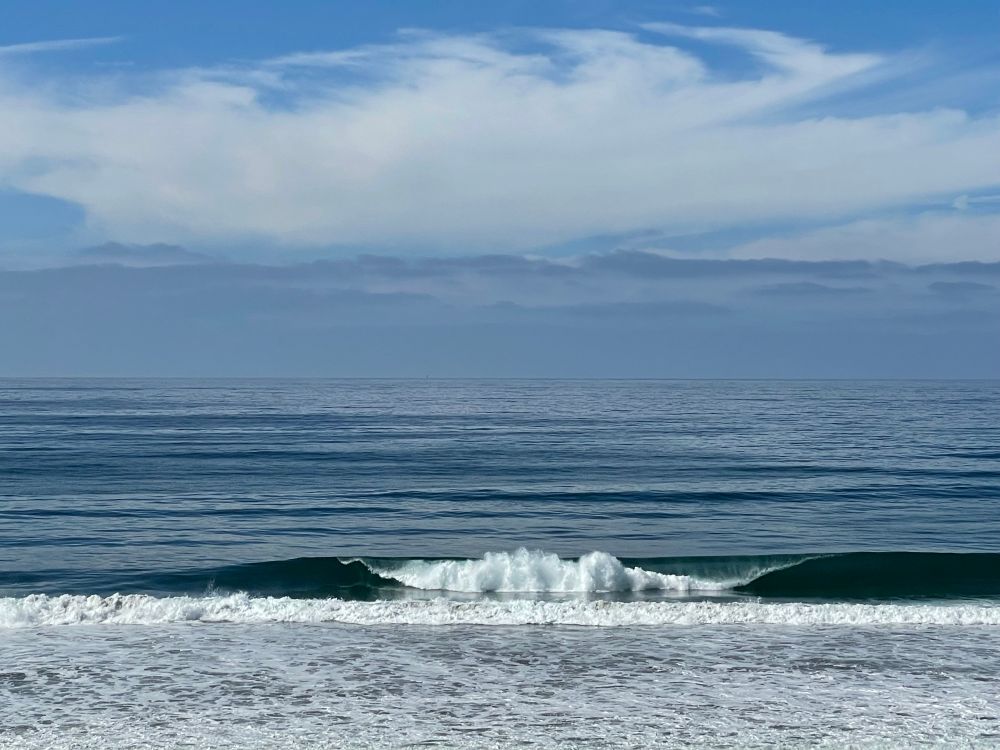A blue sky with clouds blends into the colors of the Pacific ocean.