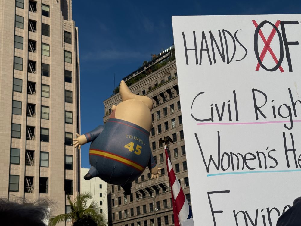 A trump balloon floats by a Hands off protest sign