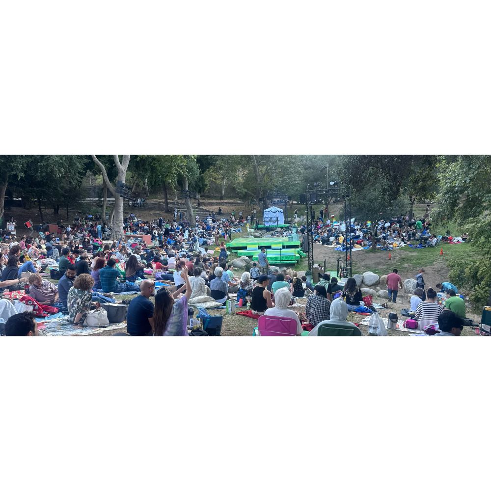 A view of the Independent Shakespeare production in Griffith Park. Hundreds of people on the grass around a green stage