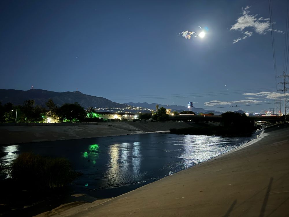 The moon shines on the LA river. The KCAL 7 TV station sign glows across the river