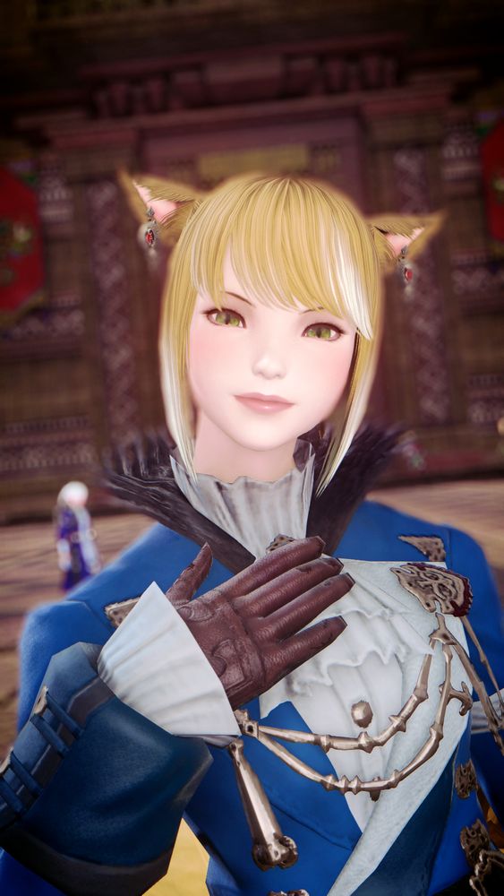 A miqo'te standing in front of the palace in Tuliyollal. She is dressed in a formal blue coat and brown gloves. In the background, you can make out a blurry Alphinaud.