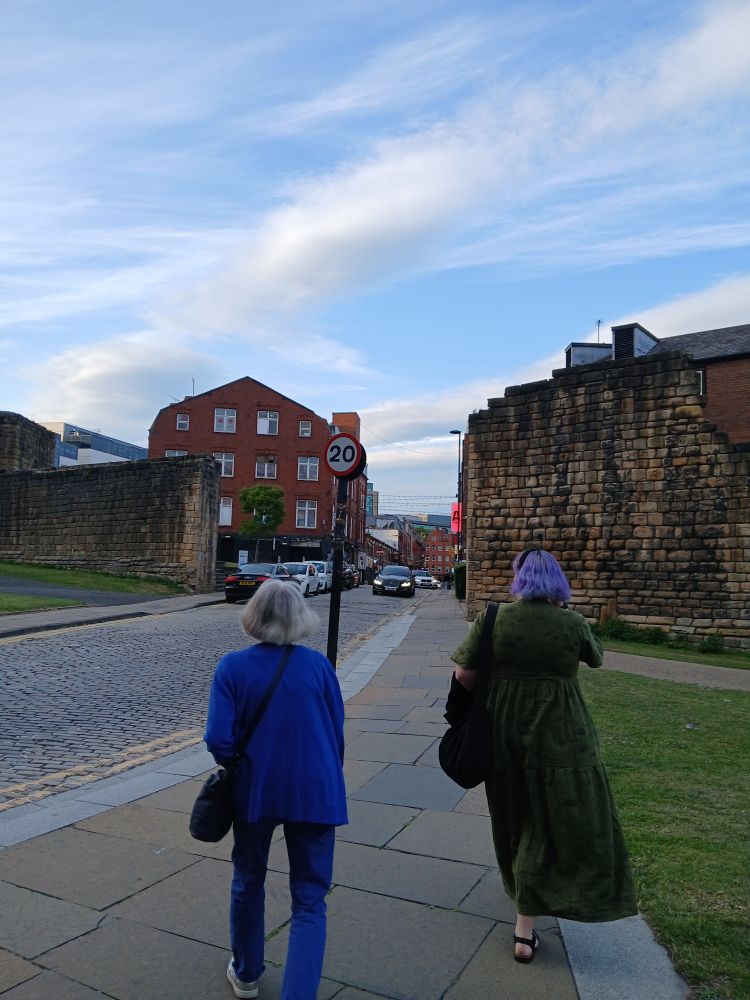 Two people walking towards one of the entrances through the Newcastle town walls. Through the entrance is China town