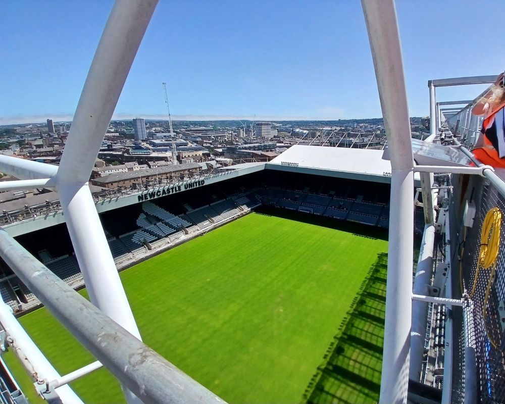 A view of an empty st james park and pitch from the roof. I am stood on the corner of the leazes end and the Milburn stand. The sky is blue and you can see the wider Newcastle area outside the stadium