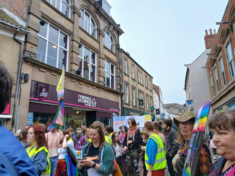 A group of people with various pride flags and signs. Some are wearing high vis jackets