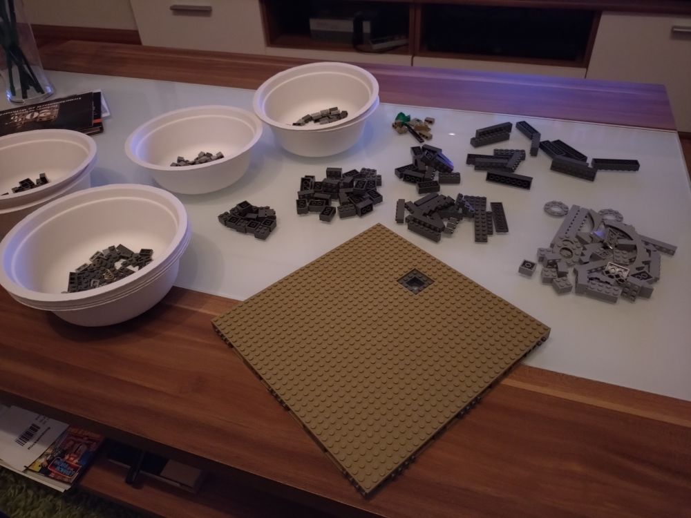 Bild zeigt eine gebaute Grundplatte, dahinter einzelne Teile in verschiedenen Grautönen und links daneben Schalen mit Kleinteilen