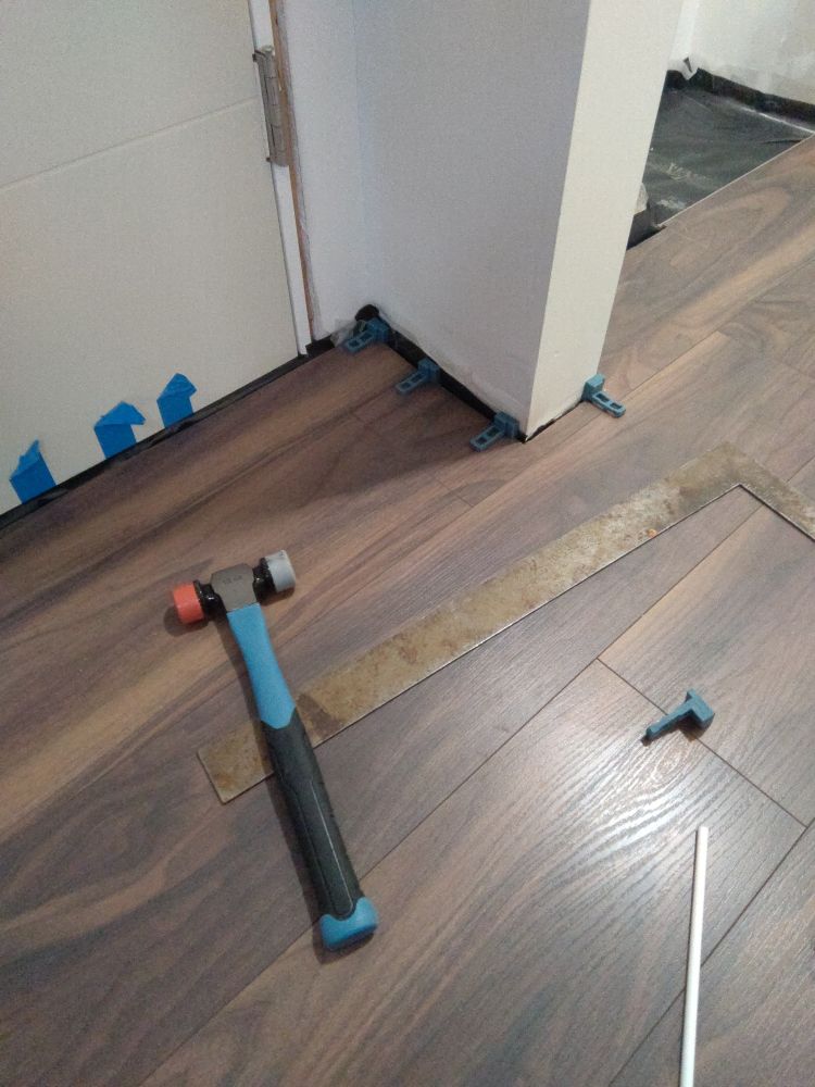 a hammer and a metal ruler sitting on top of some newly-installed flooring. There are small blue spacers along the edges of the flooring and the walls. My cuts aren't exactly straight but it's fine