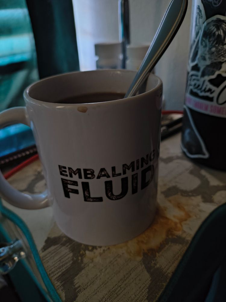 Photo of a white mug with black text reading "EMBALMING FLUID" printed onto it. 
The mug is full of hot chocolate, a custom mix of dark chocolate and instant french vanilla cappuccino, for anyone curious