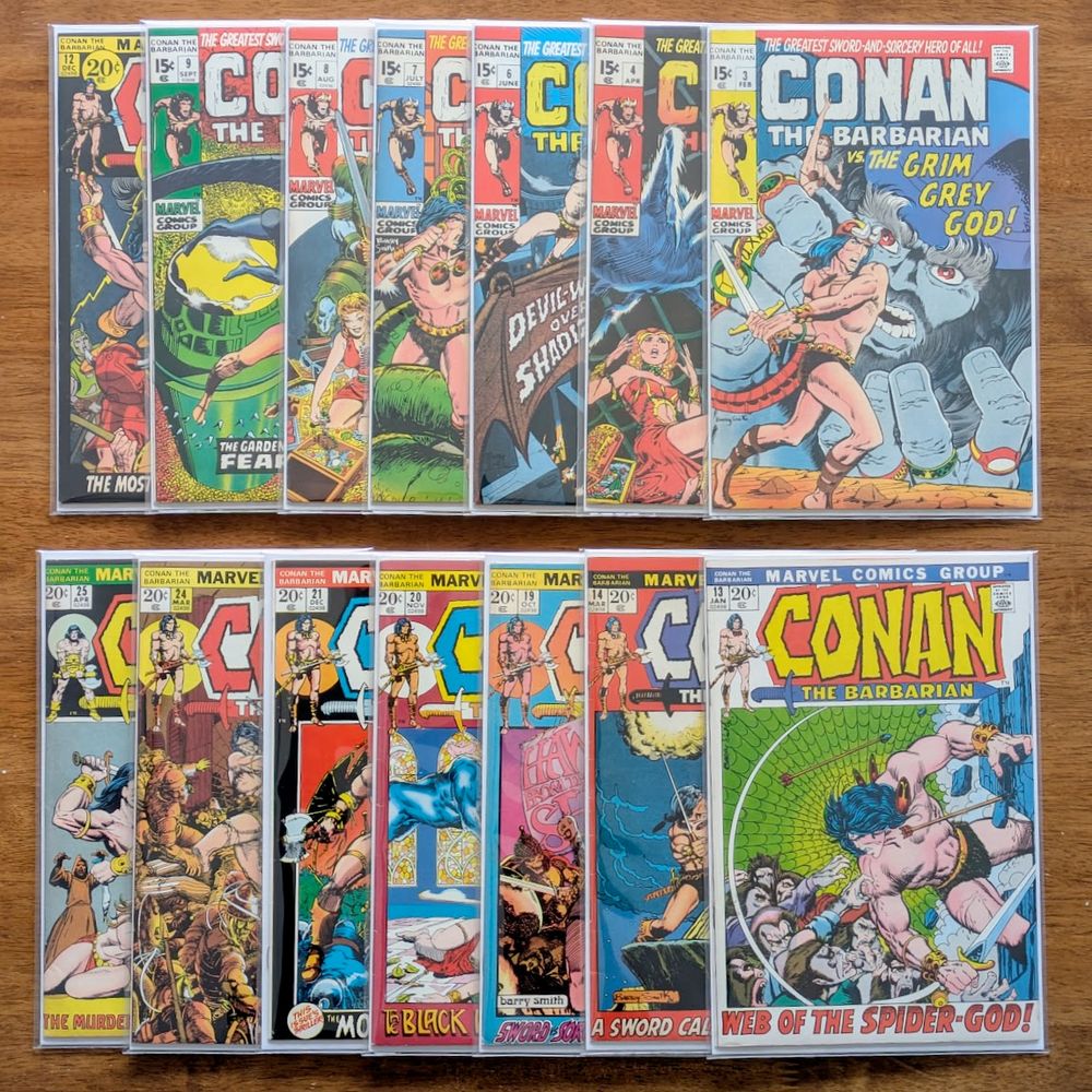 A photograph of 14 Conan The Barbarian comics books arranged on a wood table in 2 rows each of 7 overlapping books.