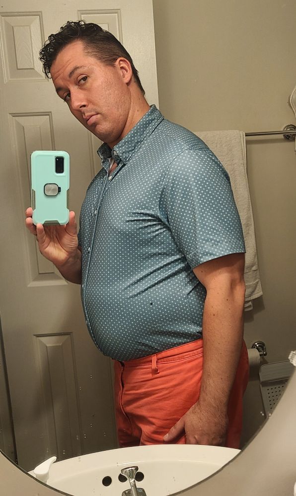 El Dad in a teal button down shirt sleeve shirt and bright red shorts. The shirt is tucked in to show his form.