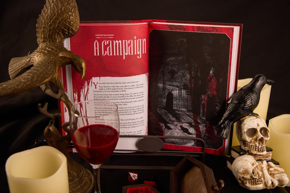 product photography of a physical copy of paint the town red surrounded by various vampire themed props like a goblet of blood, skulls, candles and a raven