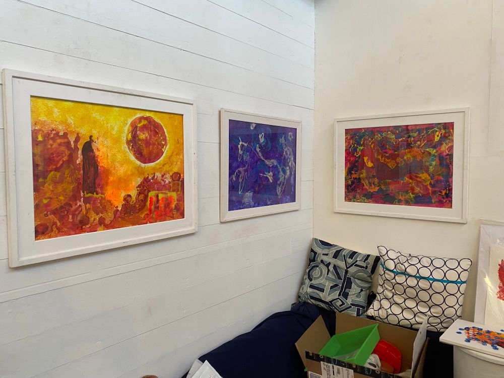 Three abstract art pieces on a wall. The art is very colorful and textural and inspired by psychedelia and science fiction