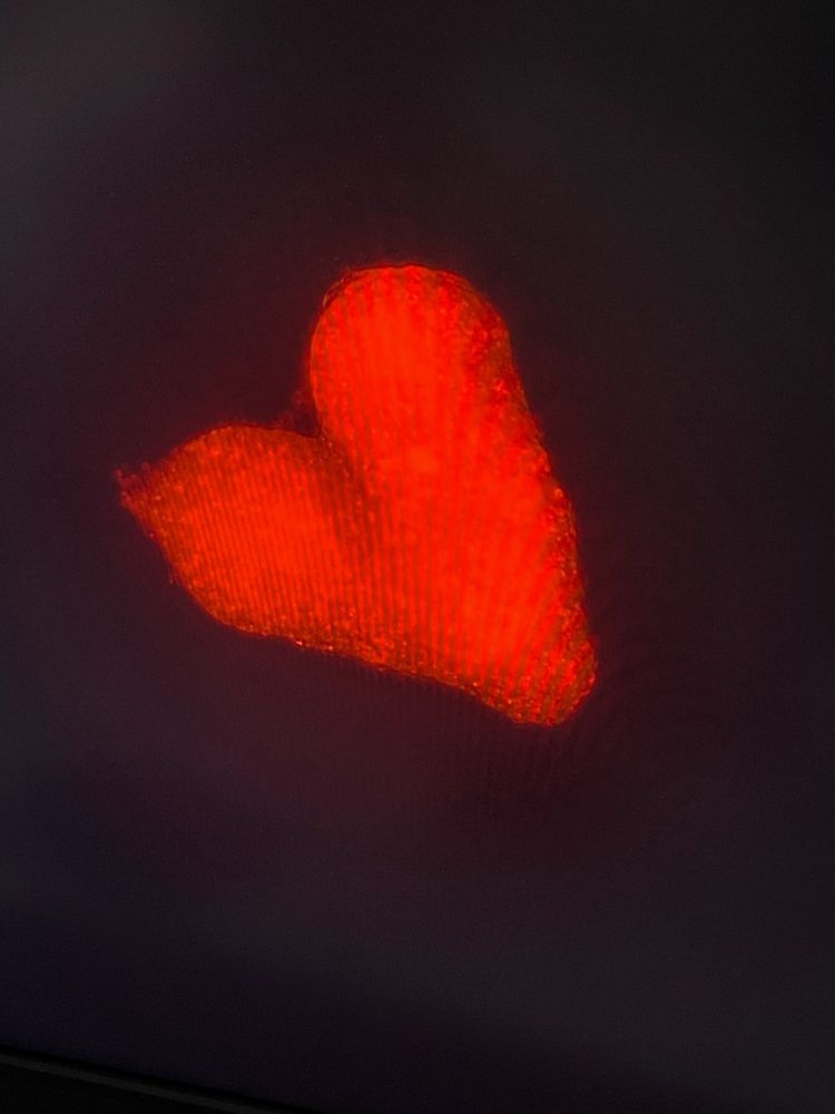 Fluorescence microscopy picture showing a red tumor spheroid in the shape of a heart on a black background 