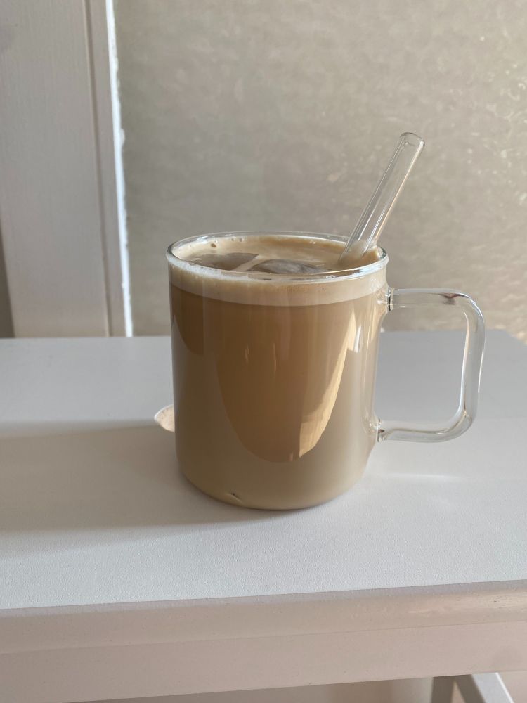 a glass mug with a glass straw filled with very milky coffee and ice cubes