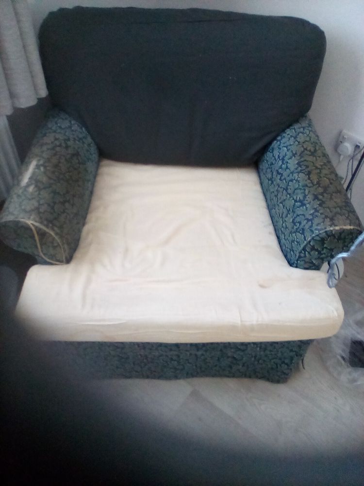 An old armchair, the original blue floral fabric has seen better days and is currently being replaced with a dark grey fabric