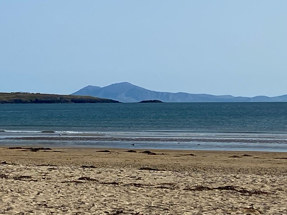 A sandy beach with blue sea and blue mountains in the background
