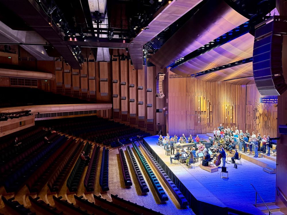 Barbican concert hall, with performers on stage rehearsing, pictured from the Circle to one side.