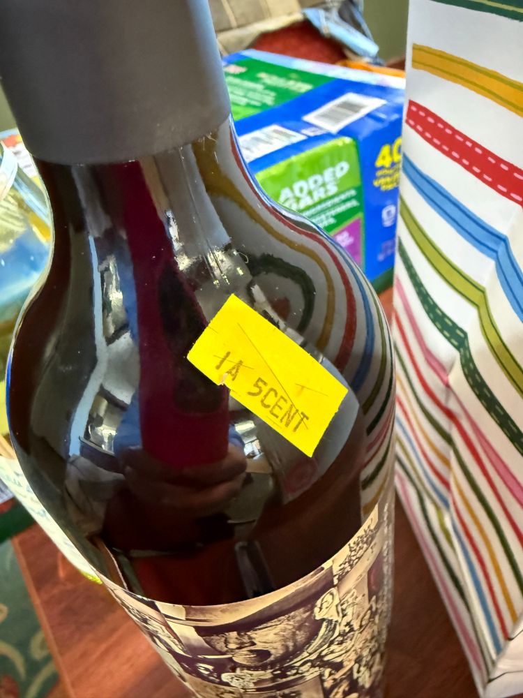 A close up picture of a bottle of wine with a yellow sticker on it that says “IA 5 cent” without a space between the 5 and the cent to make it look like scent, as in smell 