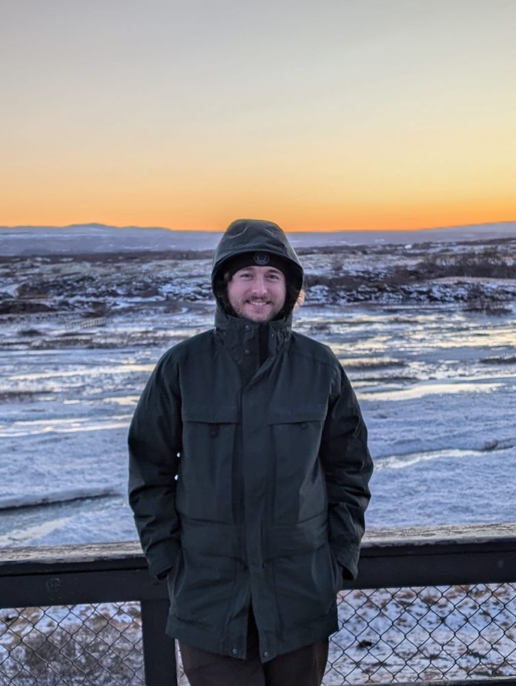 Me wearing a green coat with a fence behind me and some icy fields. Taken in Iceland. 