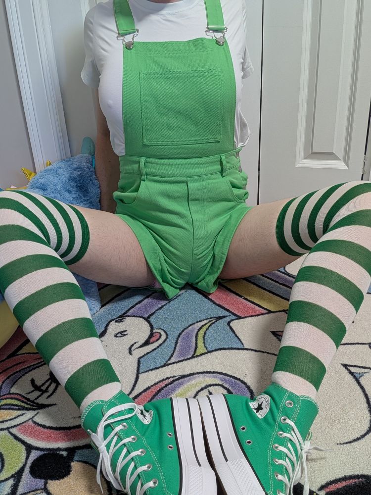 A girl in green with green converse hightops, green striped socks and green shortalls