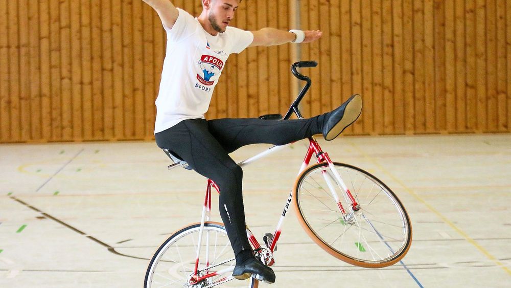 Eine Person auf einem Kunstfahrrad, die Arme von sich gestreckt und den Fuß erhoben.