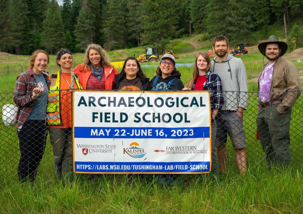 Eight people in field gear standing behind sign for the 2023 WSU archaeological field school 