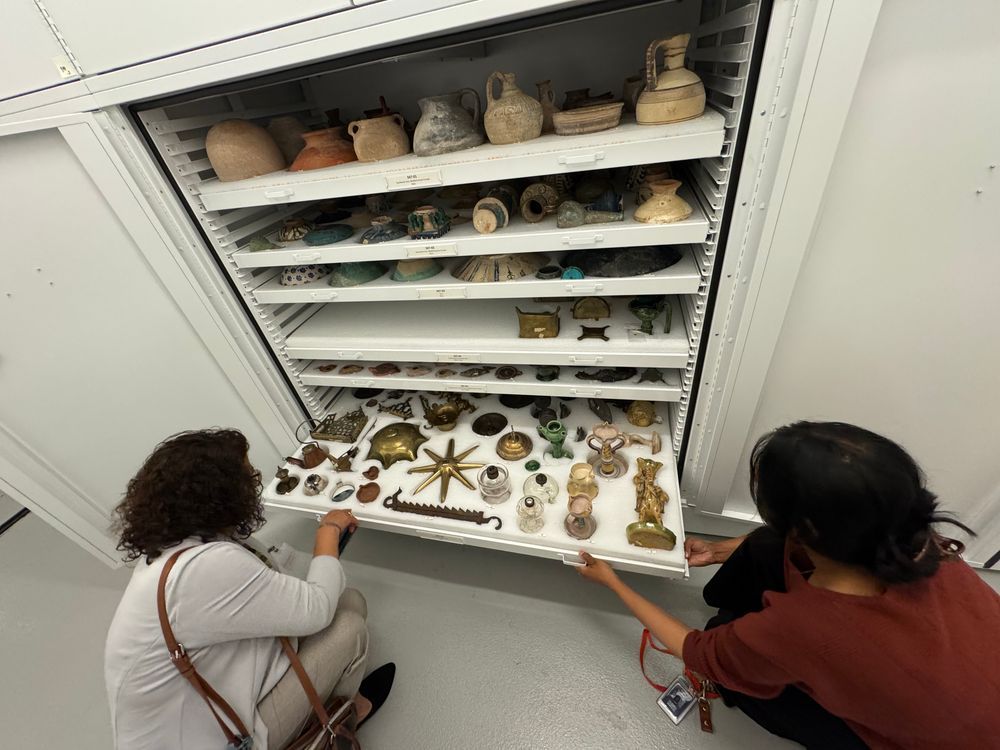 Two people looking at a drawer with an assortment of historic lamps