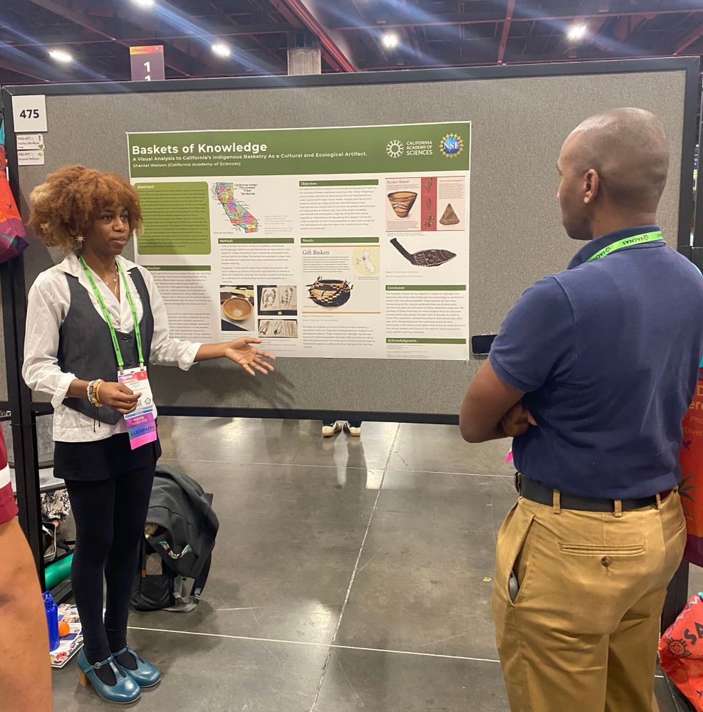 Shantel standing and explaining to a man her scientific poster presentation "baskets of knowledge"  