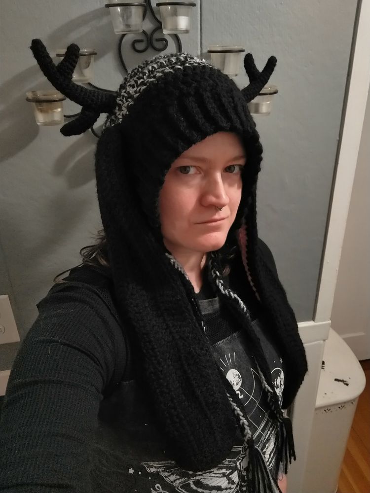 A mostly black crochet hat with lop bunny ears and antlers.