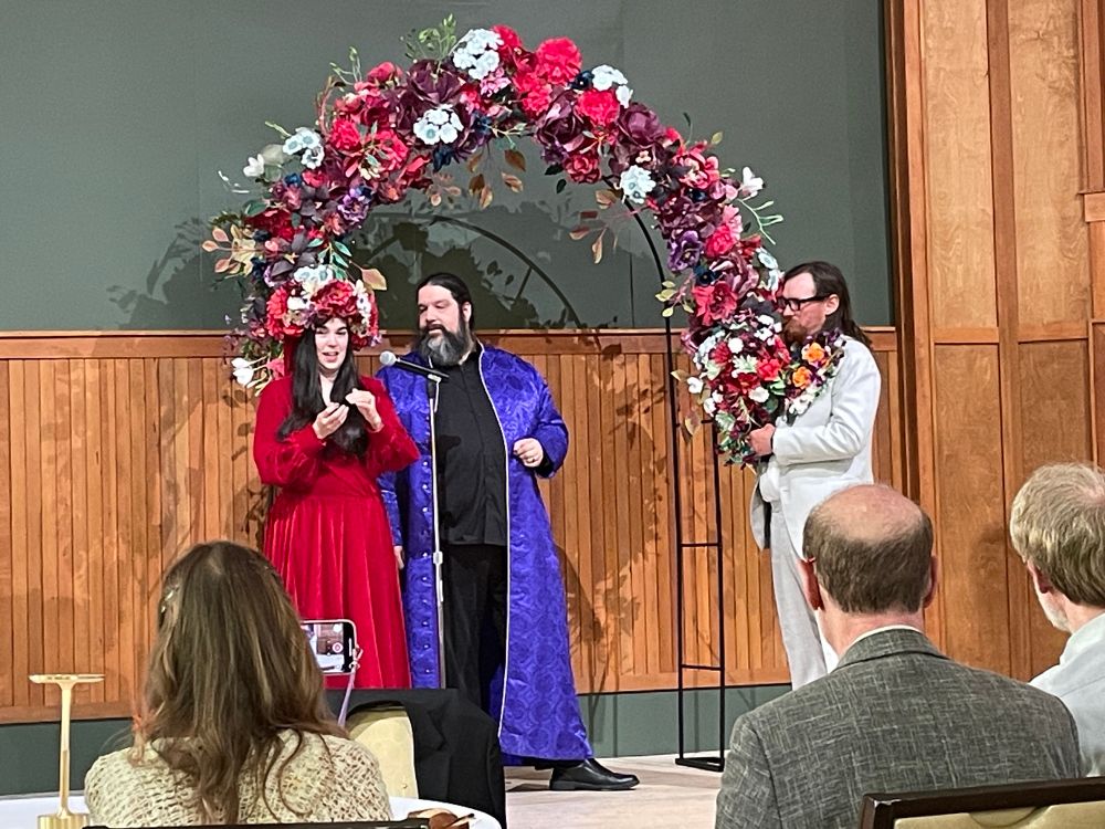 groom holds bride's bouquet while she tells the story of the stones in their wedding bands.